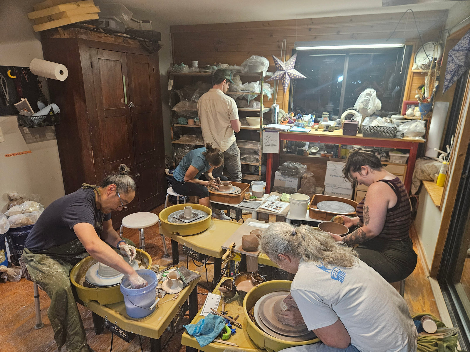 Students at their wheels in the studio, one centering clay in the foreground