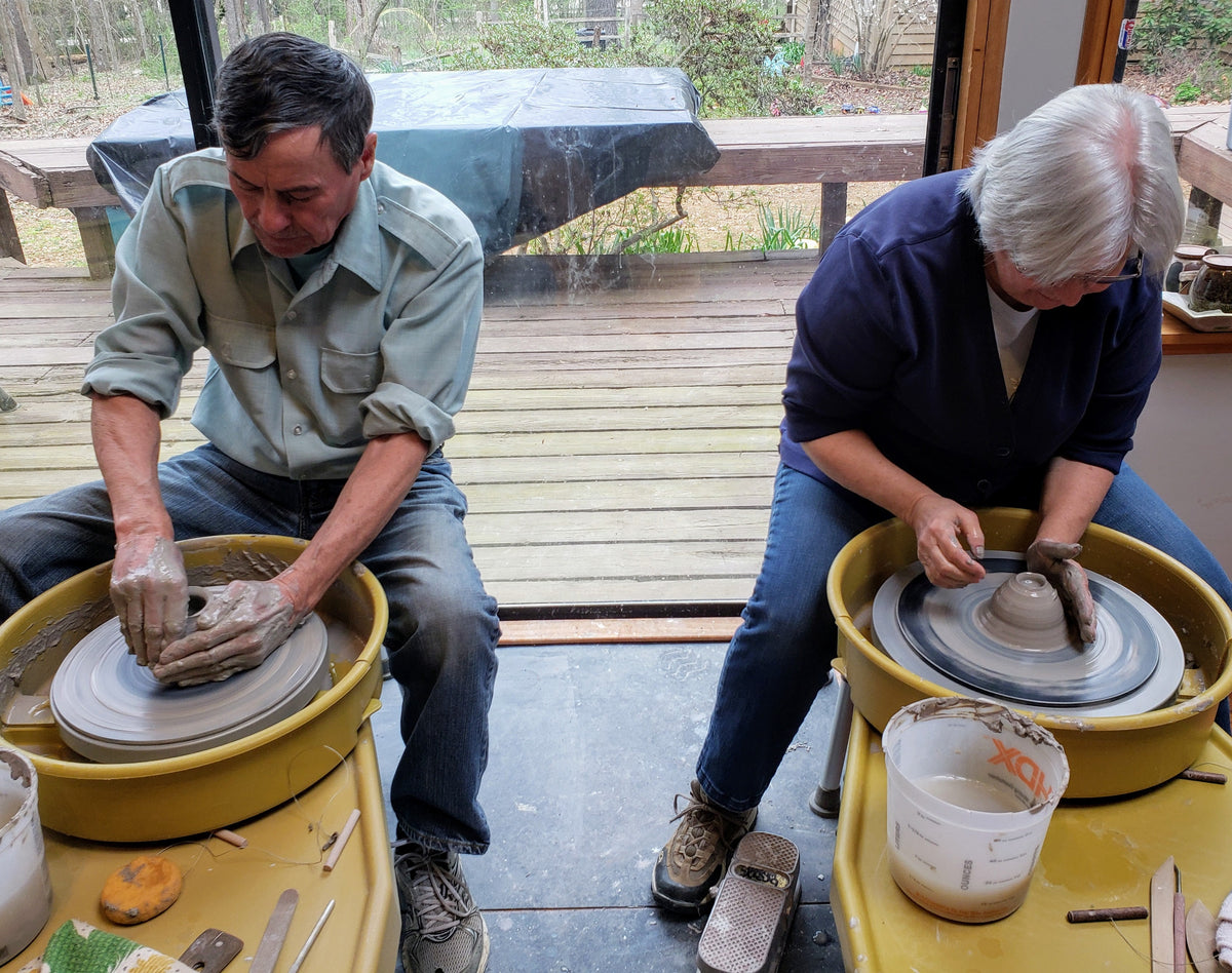 Two students at side-by-side wheels with yellow splash pans, a wooden deck behind them.